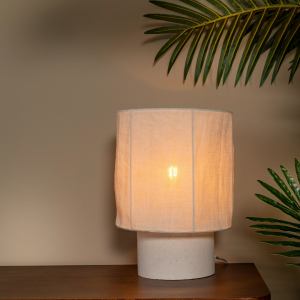 Witte stoffen tafellamp met cilindervormige voet op houten tafel in warme setting