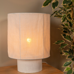 Witte tafellamp met linnen kap op houten tafel naast groene plant