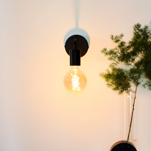 Zwarte vintage wandlamp met ronde fitting en warme gloeilamp aan muur