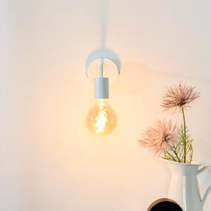 Witte vintage wandlamp met zichtbare gloeilamp naast vaas met bloemen